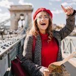 Enchanting female tourist exploring France with map. Outdoor portrait of happy brunette woman in red beret and glasses searching Paris attractions..